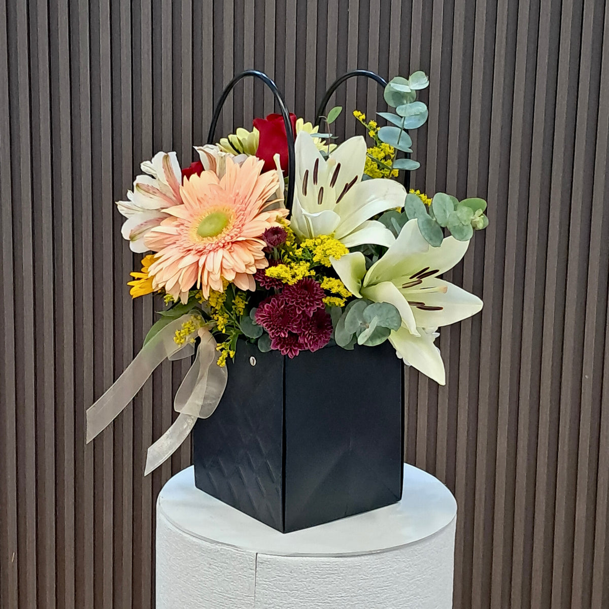 Arreglo floral multicolor en cartera negra con lazo beige de Velve Floristería, Paseo de las Flores, Heredia.