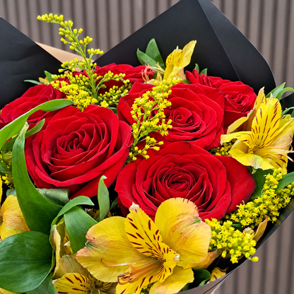Acercamiento de rosas rojas, astromelias amarillas, solidago y hojas verdes en envoltura negra. Velve Floristería, Paseo de las Flores, Heredia.