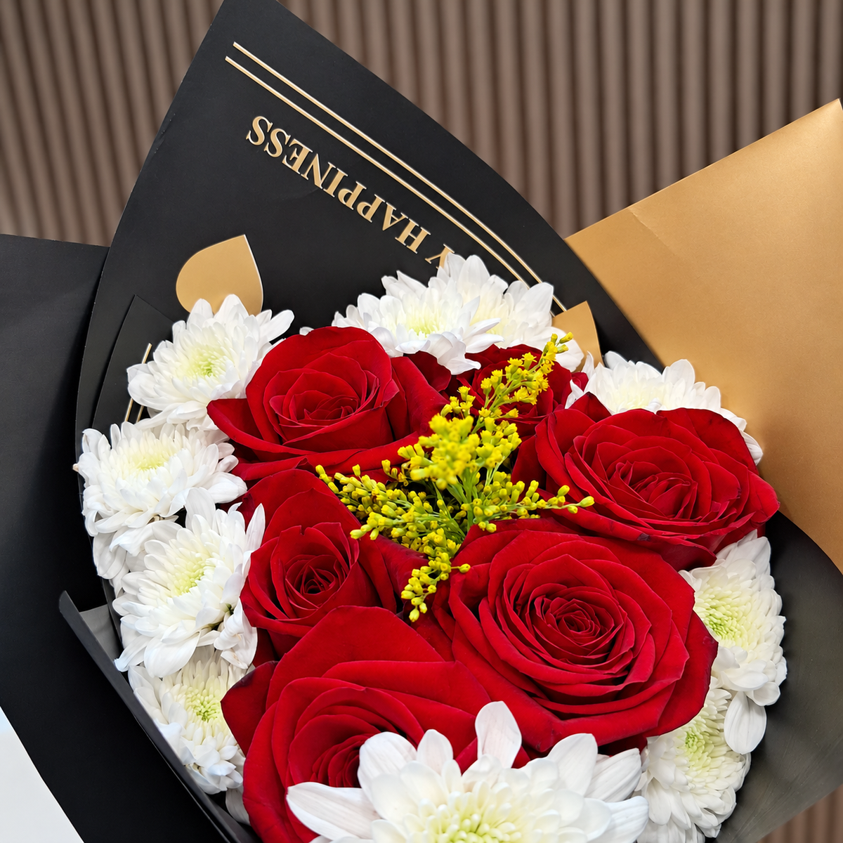 Detalle de rosas rojas rodeadas de pomas blancas y solidago amarillo en envoltura negra con corazones dorados. Velve Floristería, Paseo de las Flores, Heredia.