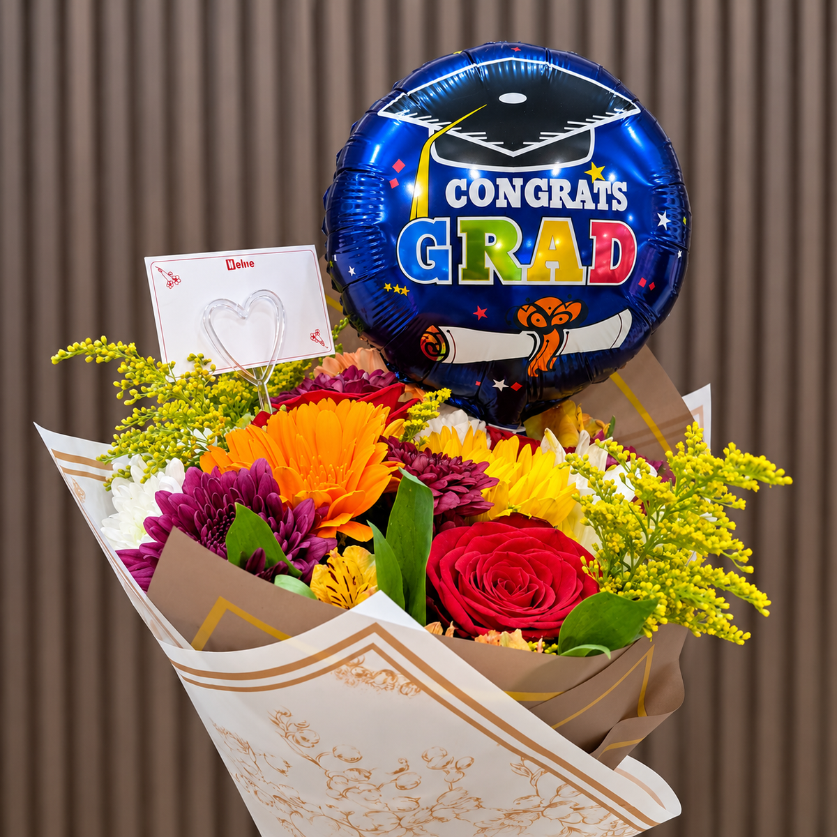 Ramo mixto de graduación con gerbera naranja, rosas rojas, girasol, crisantemos y solidago, acompañado de globo azul «Congrats Grad» y tarjeta para dedicatoria. Velve Floristería, Paseo de las Flores, Heredia.