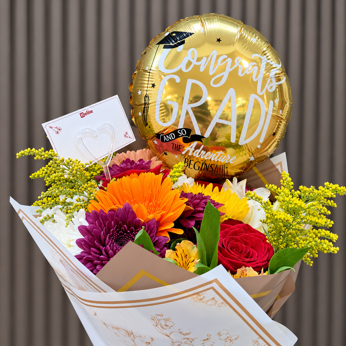 Ramo mixto de graduación con rosas rojas, gerbera naranja, girasol y crisantemos, acompañado de globo negro con letras doradas «Congrats Grad» y tarjeta. Velve Floristería, Paseo de las Flores, Heredia.