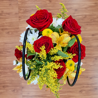 Vista cenital de canasta negra con rosas rojas, astromelias amarillas, pomas blancas y amarillas y solidago sobre piso laminado. Velve Floristería, Paseo de las Flores, Heredia.