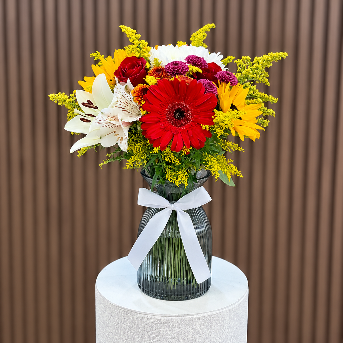 Arreglo en jarrón gris con gerbera roja, girasoles, rosas y flores blancas, vista frontal. Velve Floristería, Paseo de las Flores, Heredia.