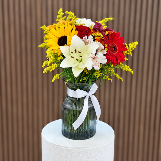 Flores mixtas con girasol, lirio blanco y gerbera roja en jarrón gris con lazo blanco. Velve Floristería, Paseo de las Flores, Heredia.