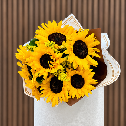 Ramo de girasoles y solidago en envoltura blanca y dorada, vista frontal. Velve Floristería, Paseo de las Flores, Heredia.