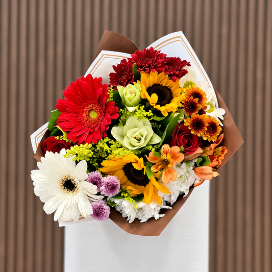Ramo mixto con girasoles, gerberas y crisantemos en envoltura blanca y café, vista frontal. Velve Floristería, Paseo de las Flores, Heredia.